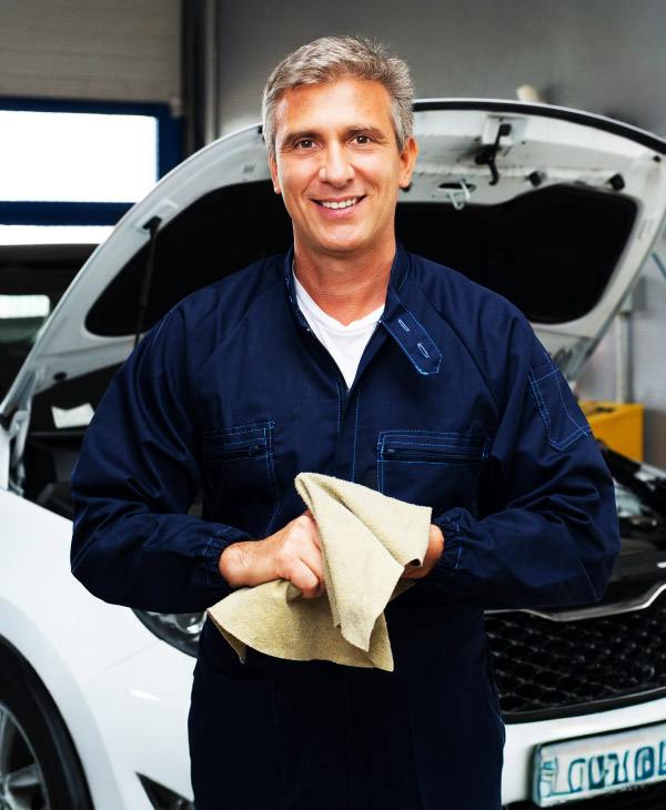 Profissional de manutenção automotiva em oficina inspecionando carro branco com capô aberto.