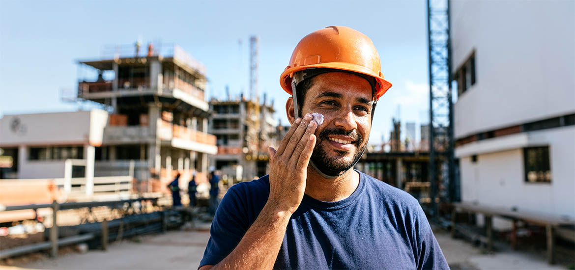 Trabalhador aplicando protetor solar no rosto antes da jornada em um canteiro de obras.